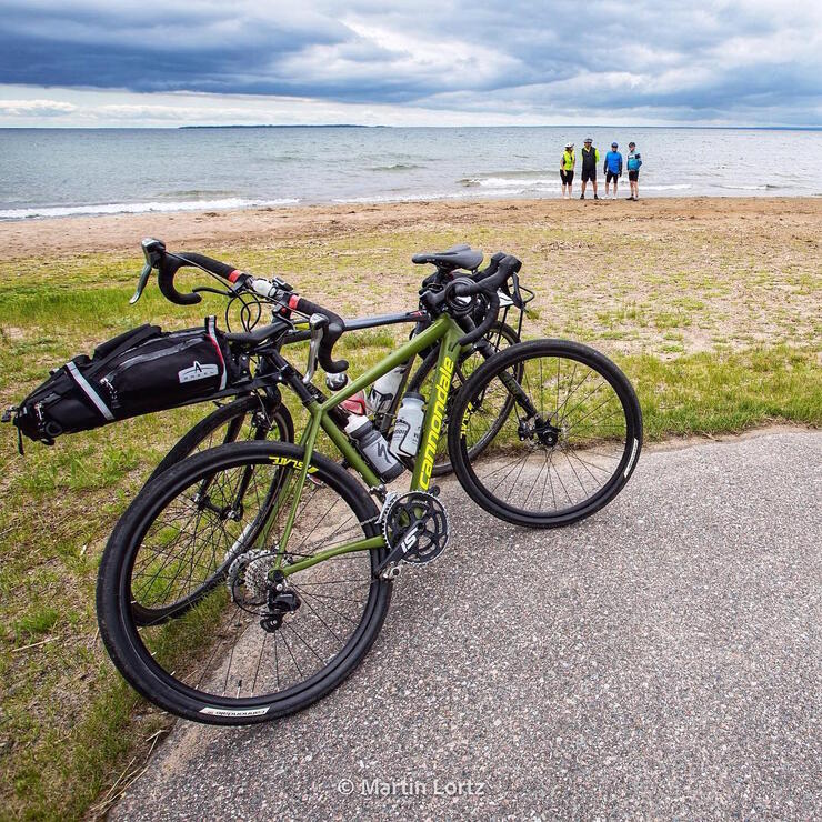 Bicycle parked along a road. Cyclists standing near the edge of a lake. 