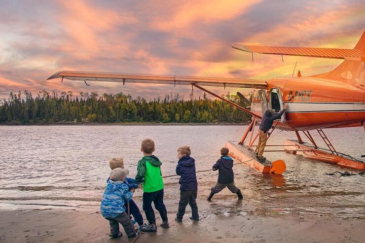 Group of kids on a beach holding a rope tied to a floatplane.
