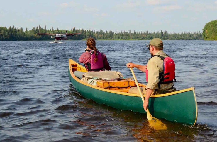 Two canoeists on lake meeting a floatplane.