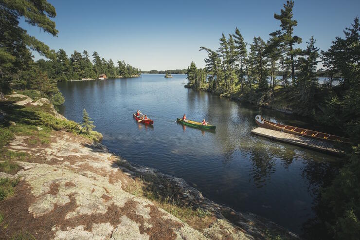Two canoes paddling up to a dock with a voyageur canoe tied to it.