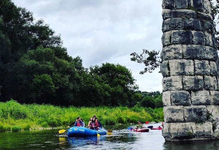 Six person raft floating by a stone pillar on the Grand River.