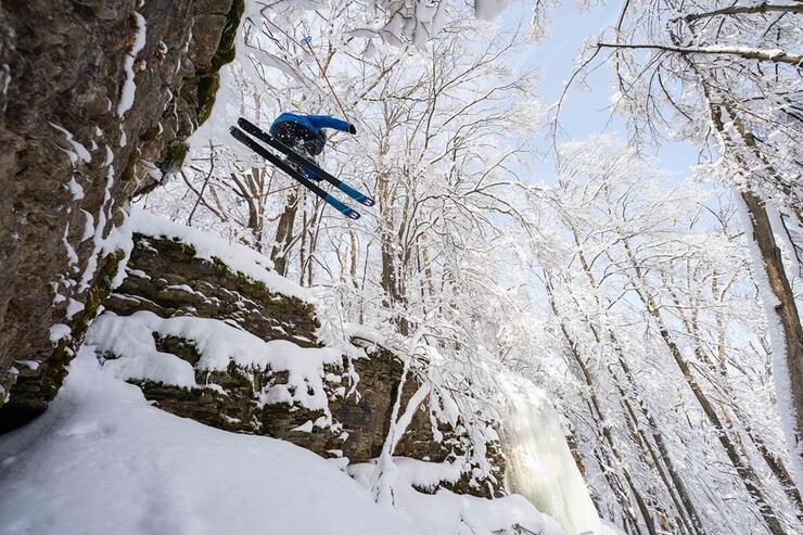 Man jumping with skiis off a rock cliff in winter.