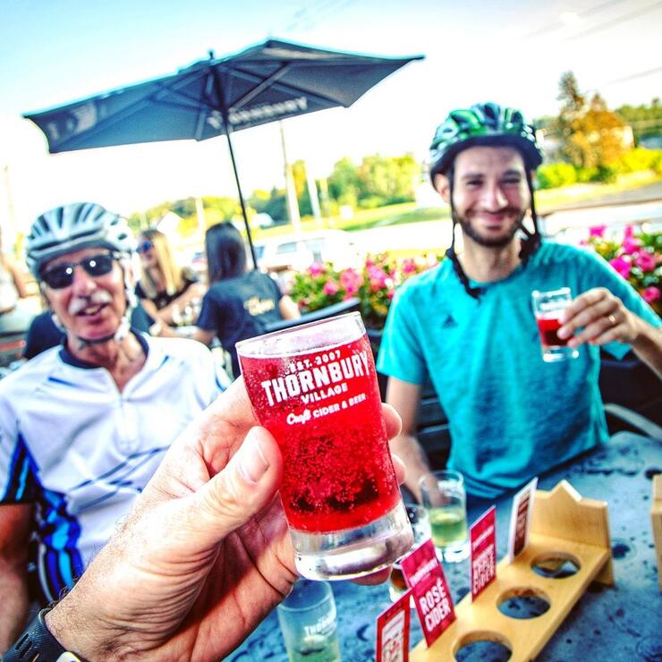 Cyclists enjoying apple cider drinks at a outdoor table. 