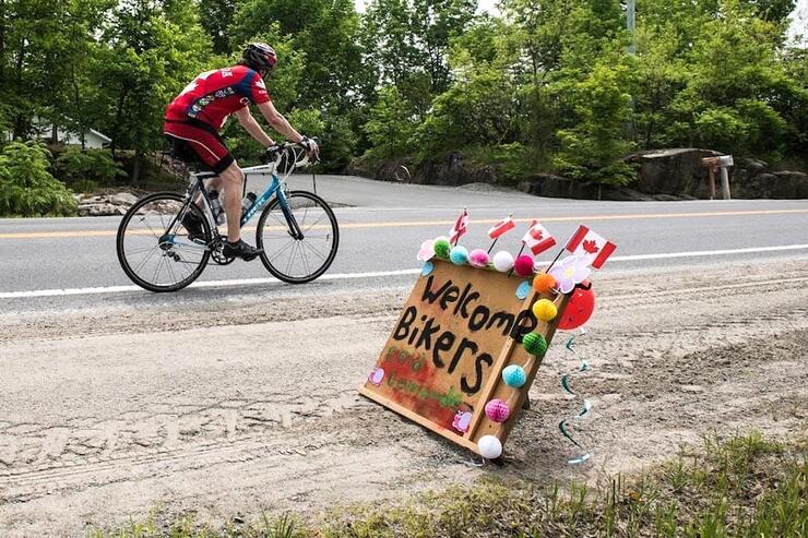 Man on a bicycle riding by a welcome bikers sign. 