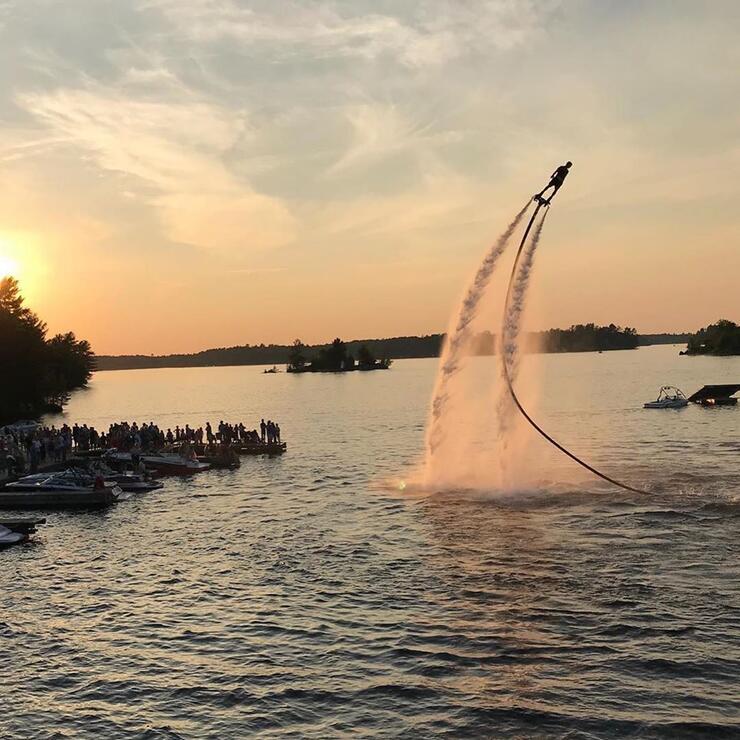 A stunt flyboarder high in the air over a lake. 
