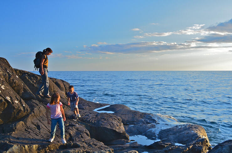 Woman and two children play on rocky shoreline