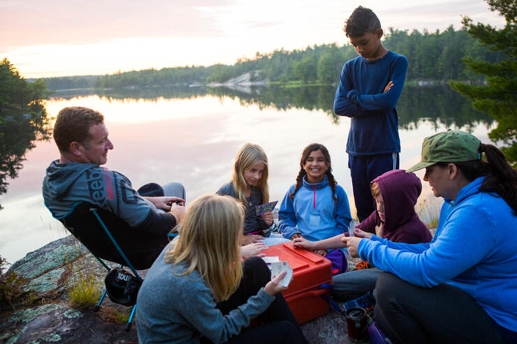 Family sitting playing cards on a rock vista overlooking a lake.