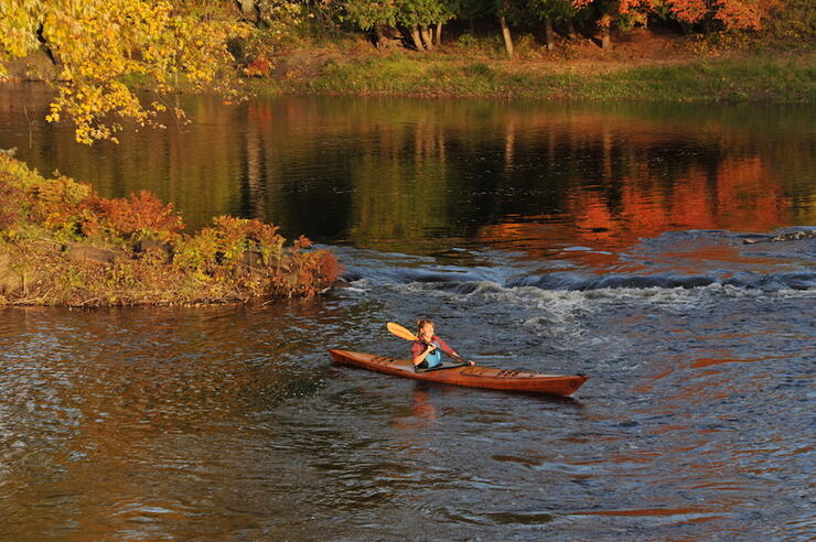 Woman kayaking on a calm river in fall.