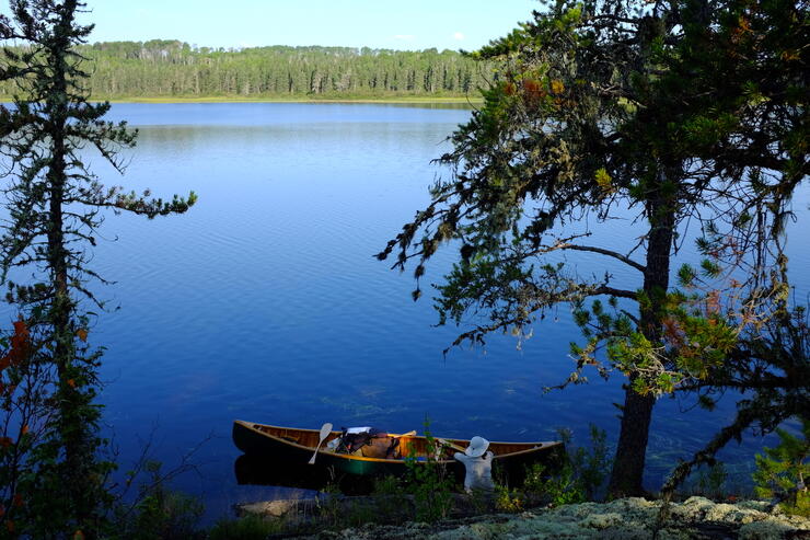 Woman on shore beside a canoe and serene lake.