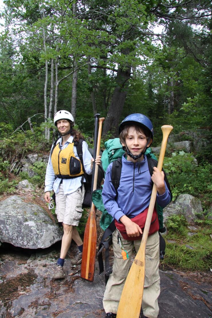 Young boy carrying a pack and paddle