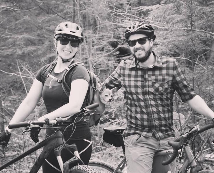 Black and white photo of a young couple standing beside their bikes. 