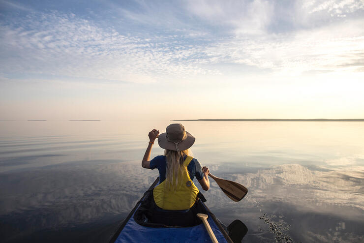 Person in bow of canoe paddling on a calm lake with blue skies above.