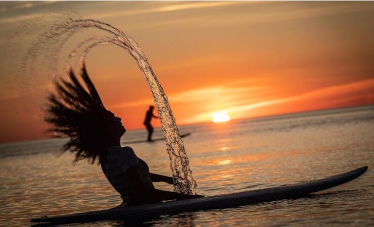 Woman flipping long hair while sitting on a paddleboard at sunset.