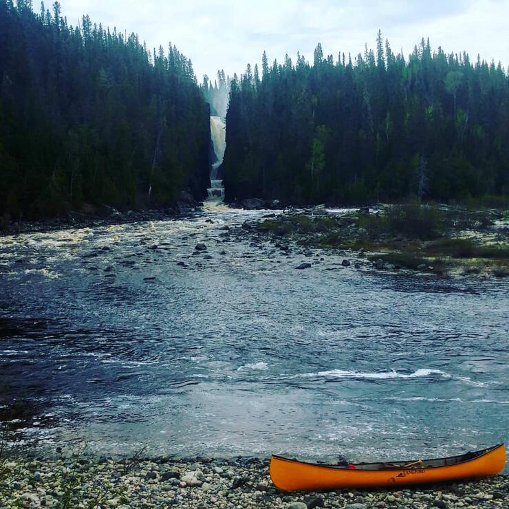 Canoe beside large pool of water at bottom of large waterfalls. 