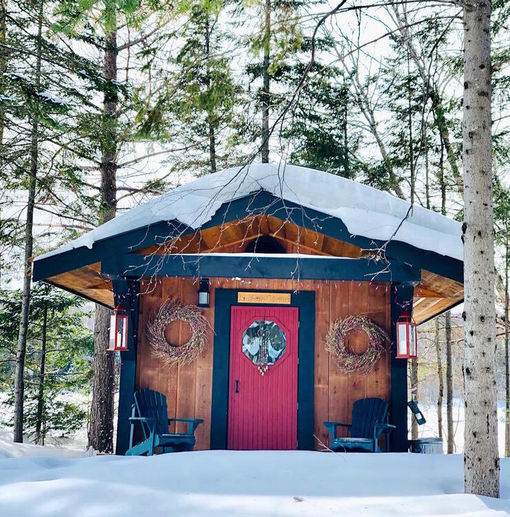 Cedar sauna cabin with a red door surrounded by snow. 