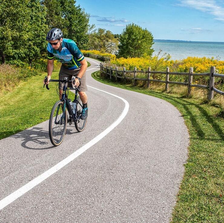 Man riding a bicycle on a paved path beside a lake.