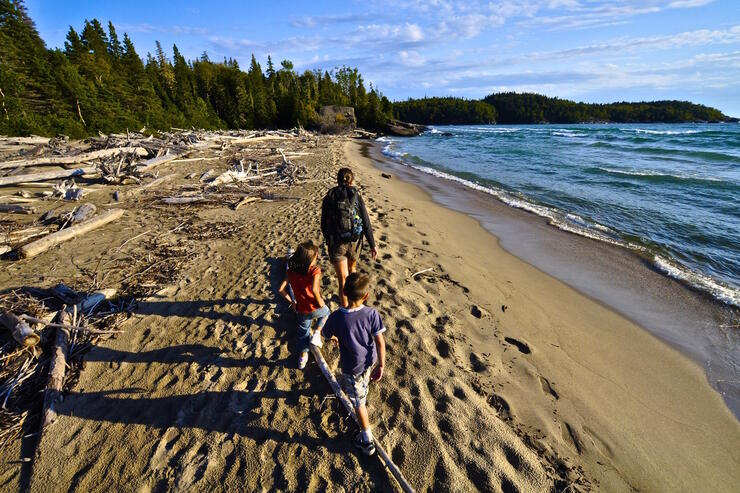 Woman and two kids hiking along a beach covered in driftwood.