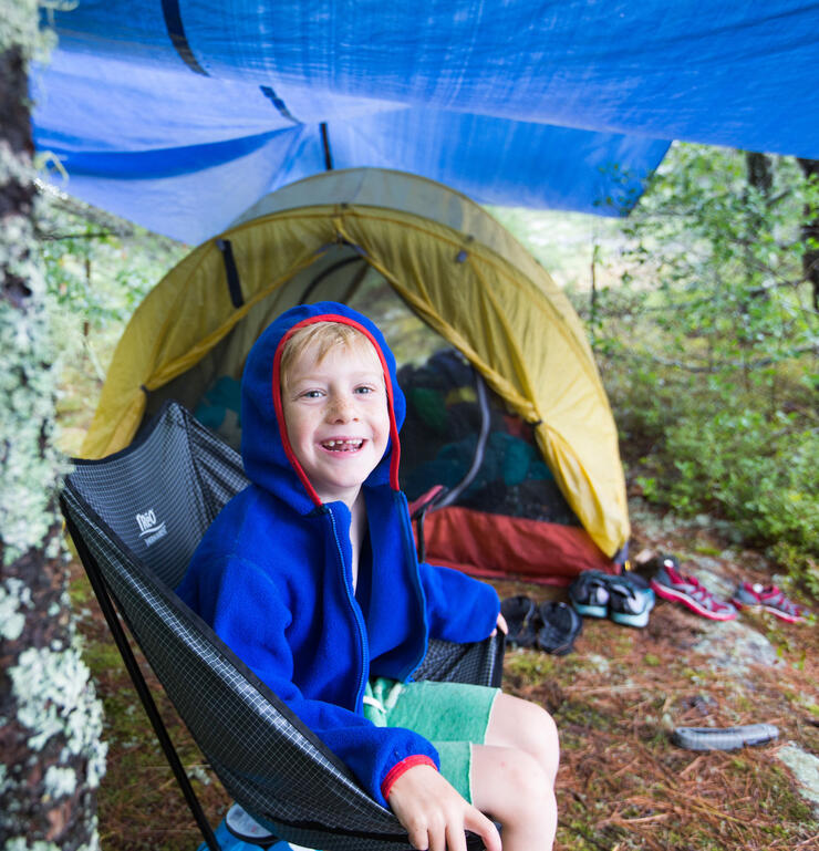 A smiling young boy sitting under a tarp.