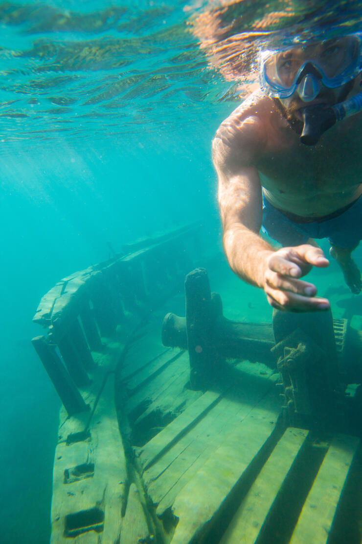 Man with mask and snorkel underwater looking at a ship wreck. 
