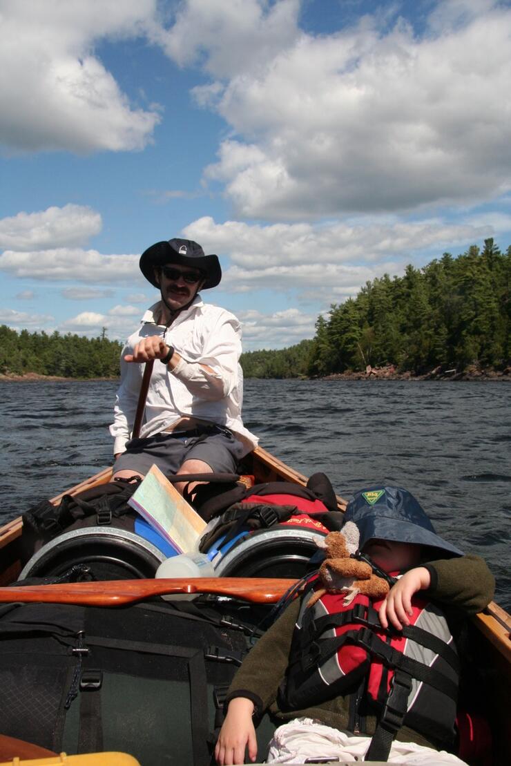 Man paddling a canoe with child sleeping in centre of canoe