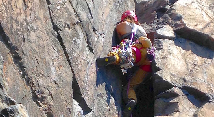 People climbing a rock face along a rock shelf.