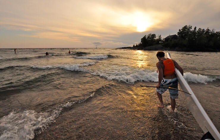 Guy carrying a SUP board into Lake Superior at sunset 
