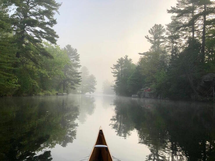 Bow of canoe travelling on a misty river.