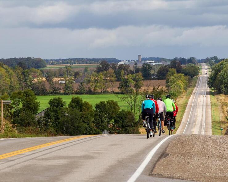 Cyclists riding over a rolling hilly paved roadway. 