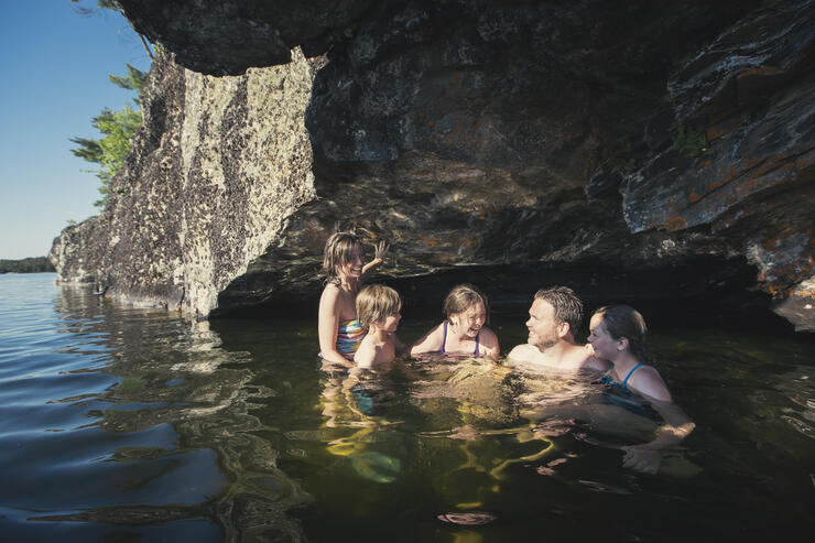Man, woman and three children swimming under a rocky outcrop.
