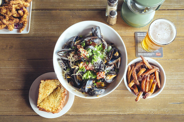 Bowl of oysters, bread, french fries and a beer on a table.