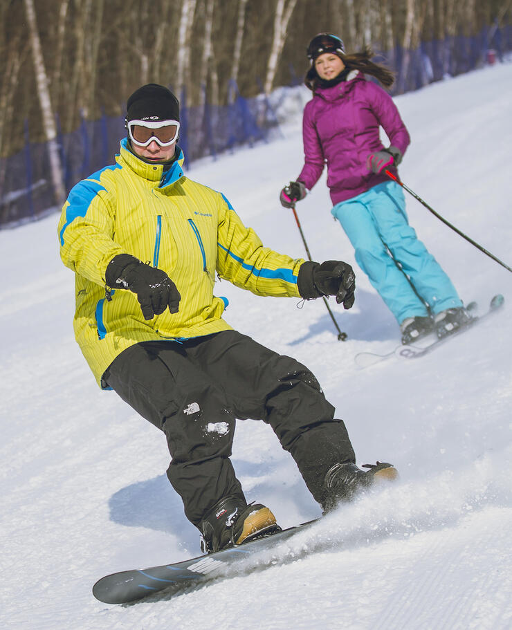 Young man snowboarding and young woman skiing