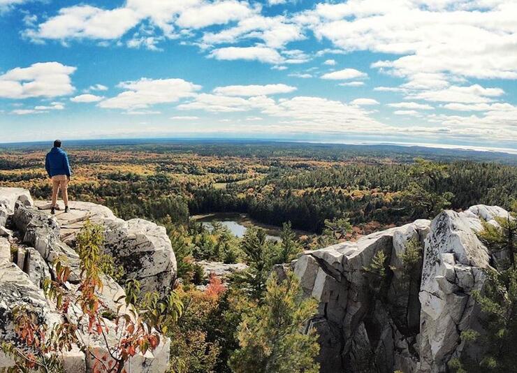 Man standing on high rock overlooking forests and lakes of Killarney.