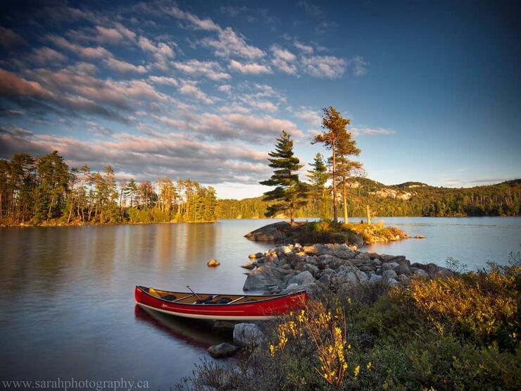 Red canoe on a rocky shoreline on a serene lake.