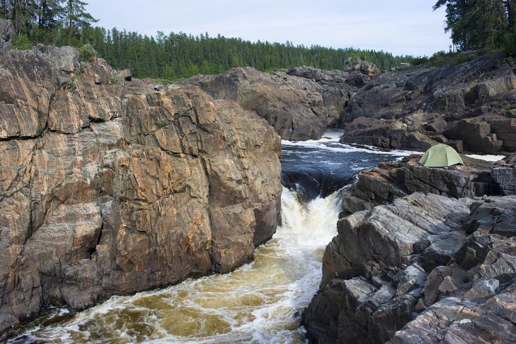Tent camped beside a large thundering waterfalls.