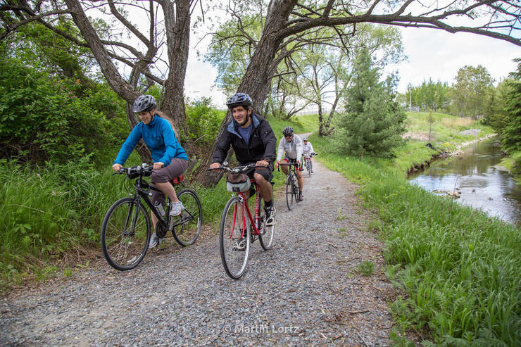 Cyclists riding on a gravel path beside a river.
