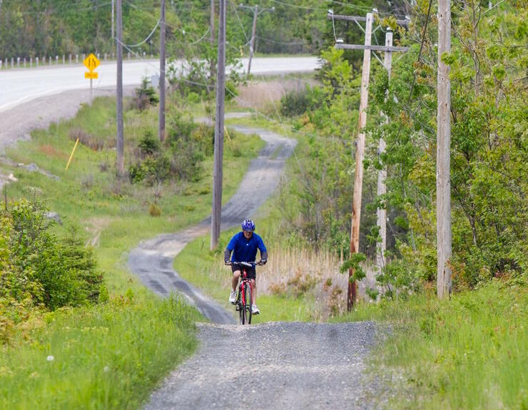 A cyclists riding up a hill on a gravel path beside a highway