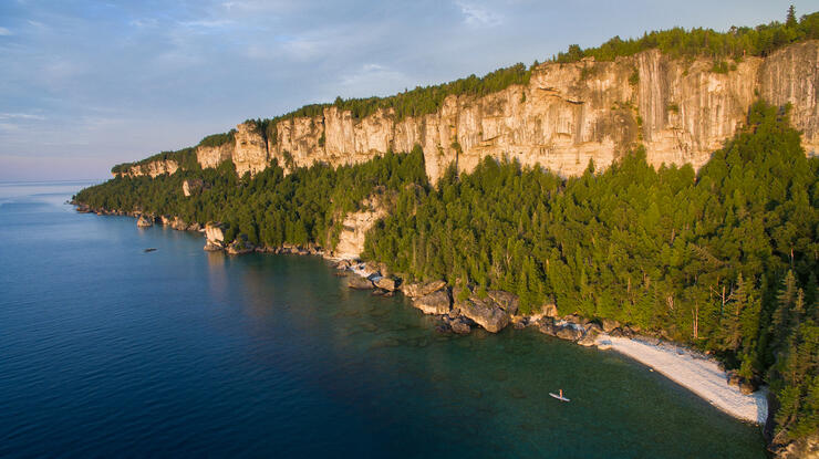 View of landscape with towering rocky cliffs, white sand beach and a SUP on turquoise water
