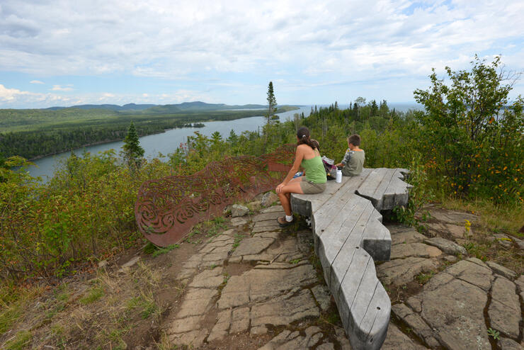 Woman and child sitting on wooden bench shaped like a finger 