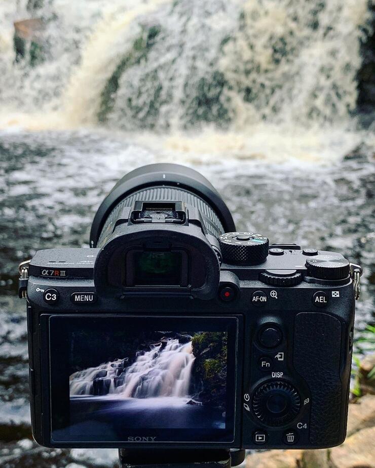 Close up of back of digital camera with cascading water in front of a waterfall.