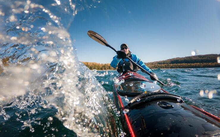 Man sea kayaking in red kayak with a big water splash.