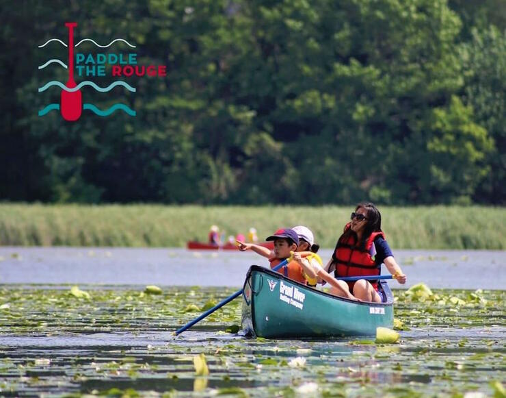 Woman and two children paddling a green canoe in lily pads on Rouge River.