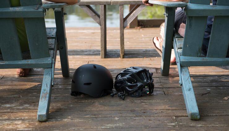 Two bicycle helmets on a deck between two wooden chairs. 
