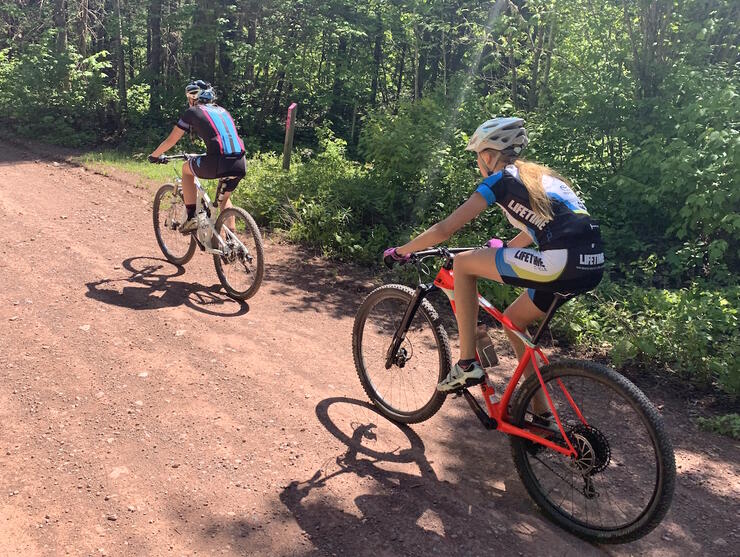 Two cyclists riding on a gravel road. 