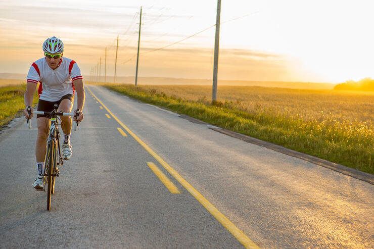 Cyclist riding on paved highway surrounded by fields.
