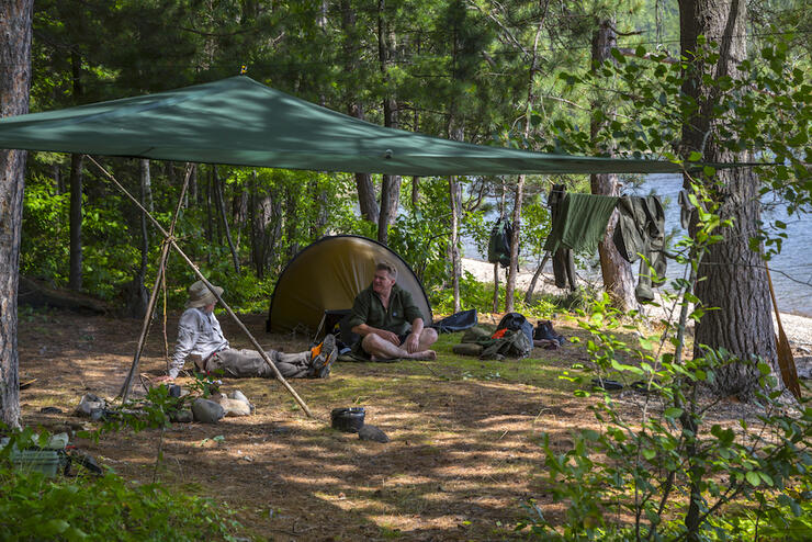 two men sitting on ground at a campsite 