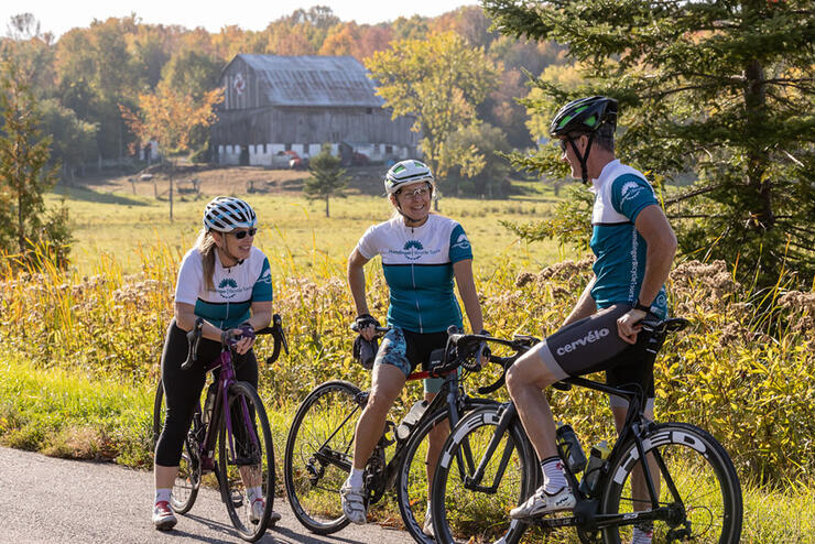 three cyclists on a guided tour stop for a break in front of picturesque barn in fall