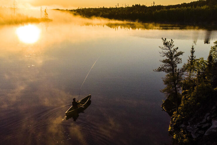 Person canoeing on lake as mist rises up