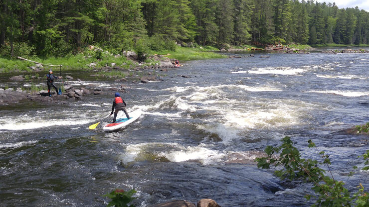 person receives instruction while balancing on a standup paddleboard in whitewater