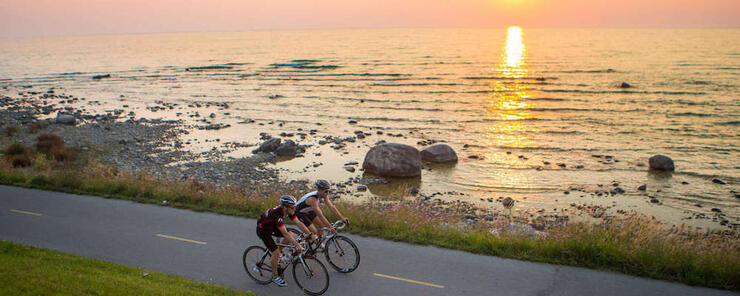 Two cyclists riding on paved trail next to water