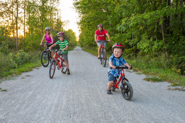 Mother, father and two young children on bicycles on rail trail.